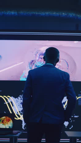 Anonymous-flight-director-in-suit-walking-towards-big-screen-with-astronaut-during-remote-spacecraft-launch-in-control-center.-Vertical-shot.